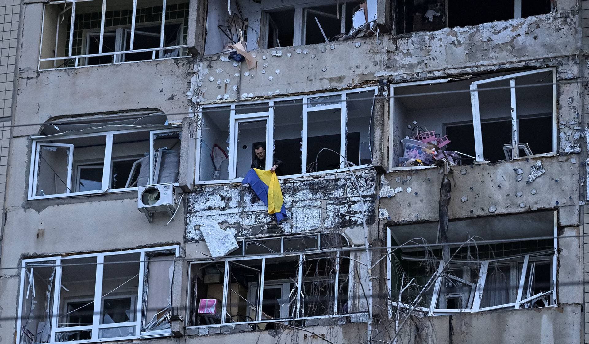 A resident hangs the Ukrainian national flag on his balcony in an apartment building hit by Russian drone in Lviv