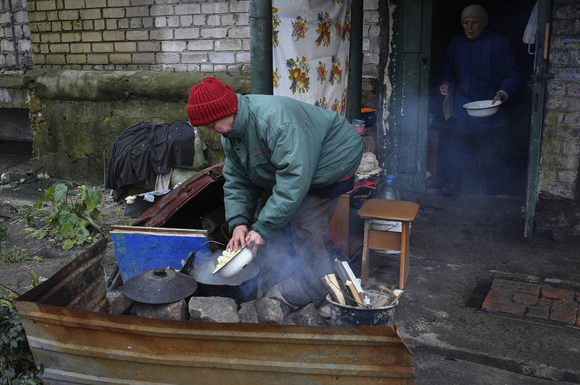 Elderly women cook food on a fire in the yard of an apartment building in Lyman