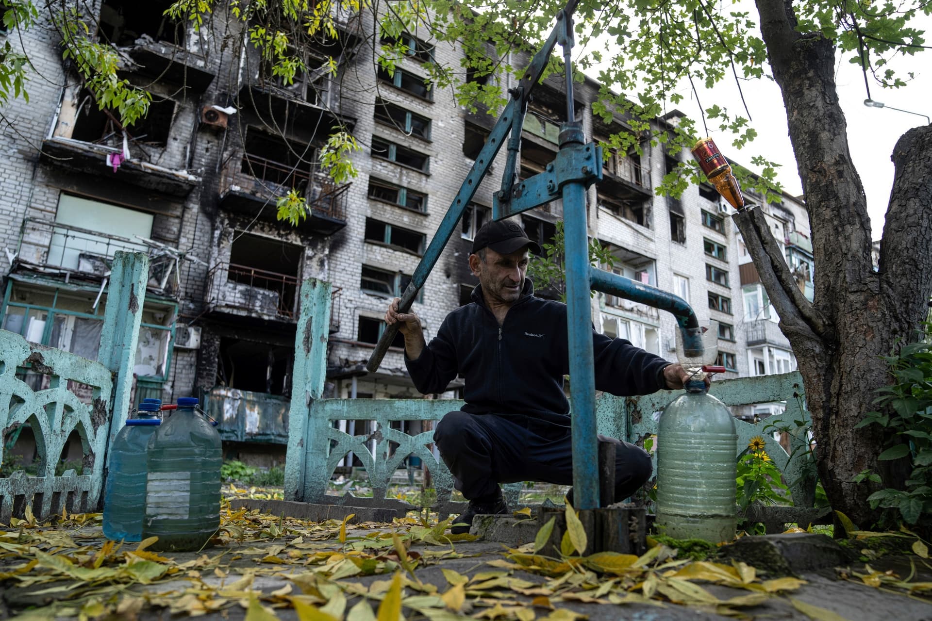 A man pumps water in front of destroyed house in the recently recaptured town of Lyman