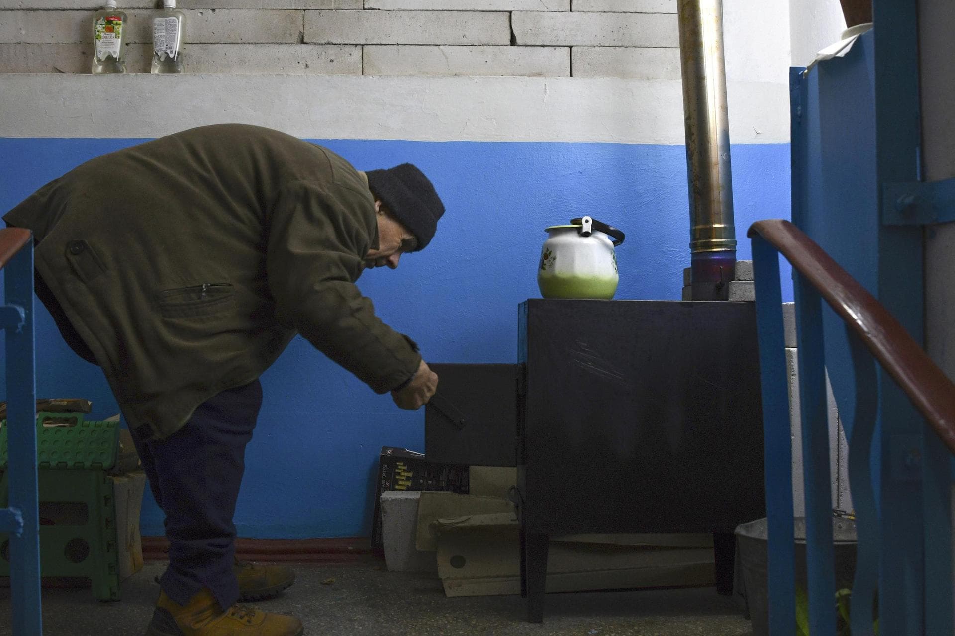 A man cooks food on a potbelly stove on the stairs entrance of an apartment building in Lyman