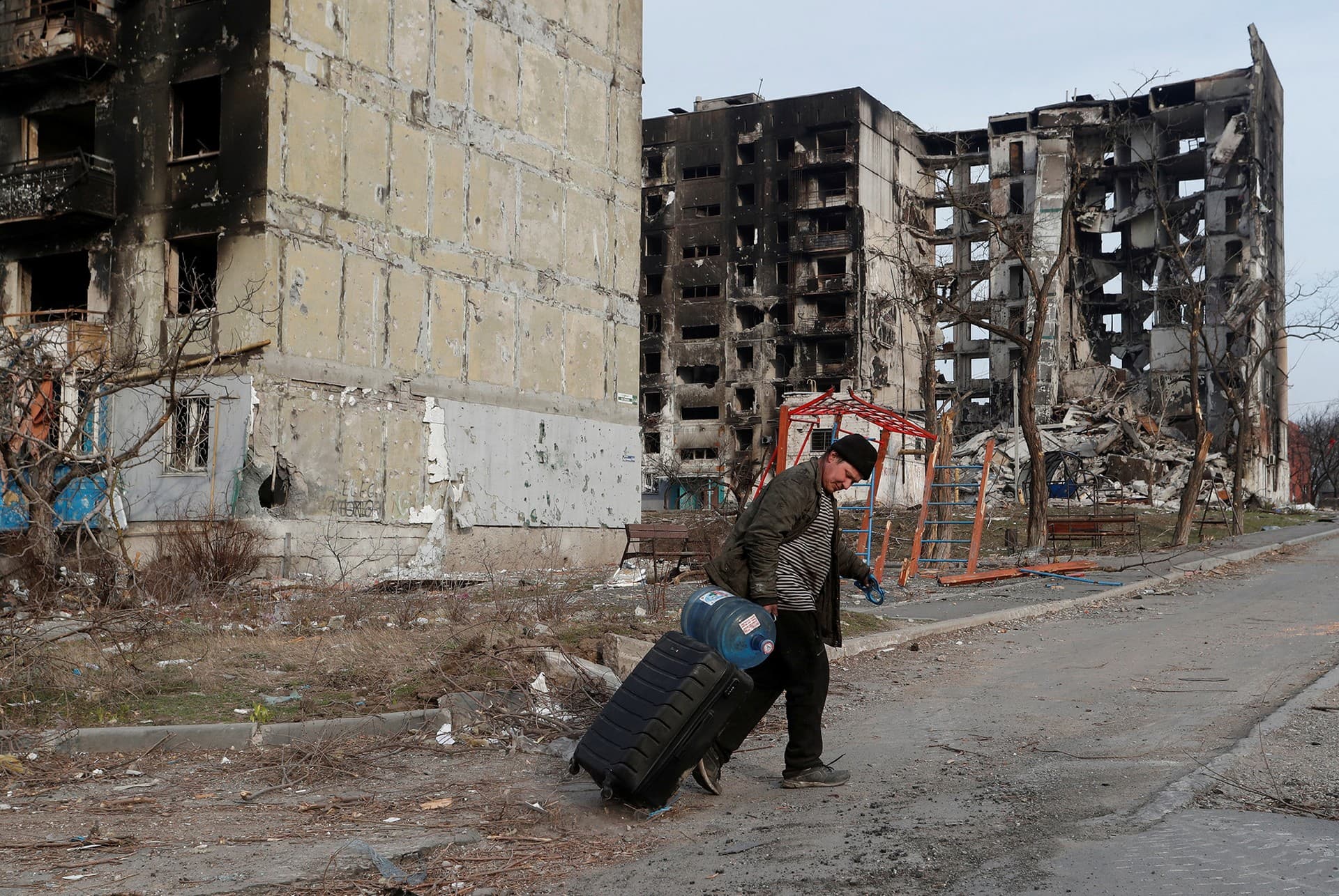 A local resident walks with a suitcase past destroyed apartment buildings in Mariupol