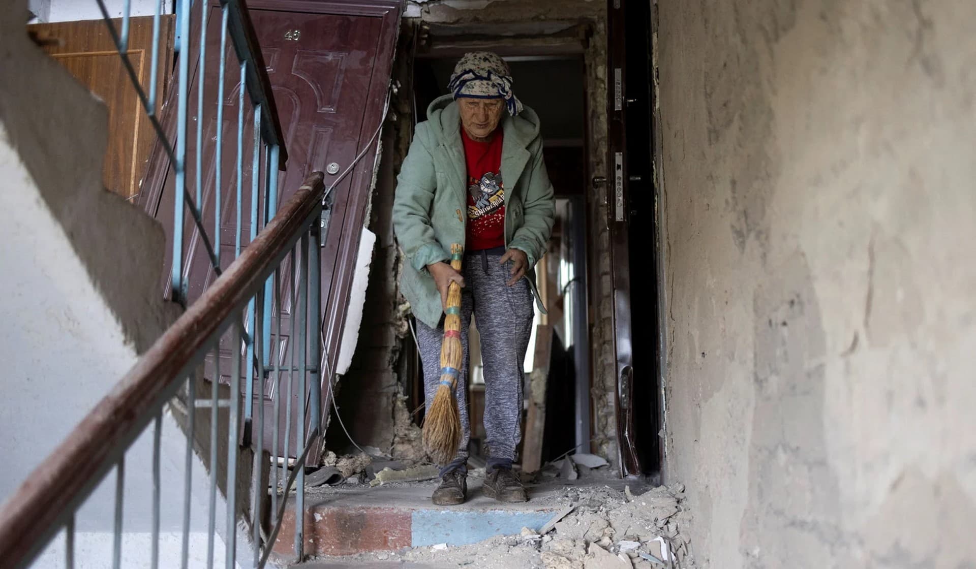 A woman cleans the entrance of a residential building destroyed by a strike in Mykolaiv