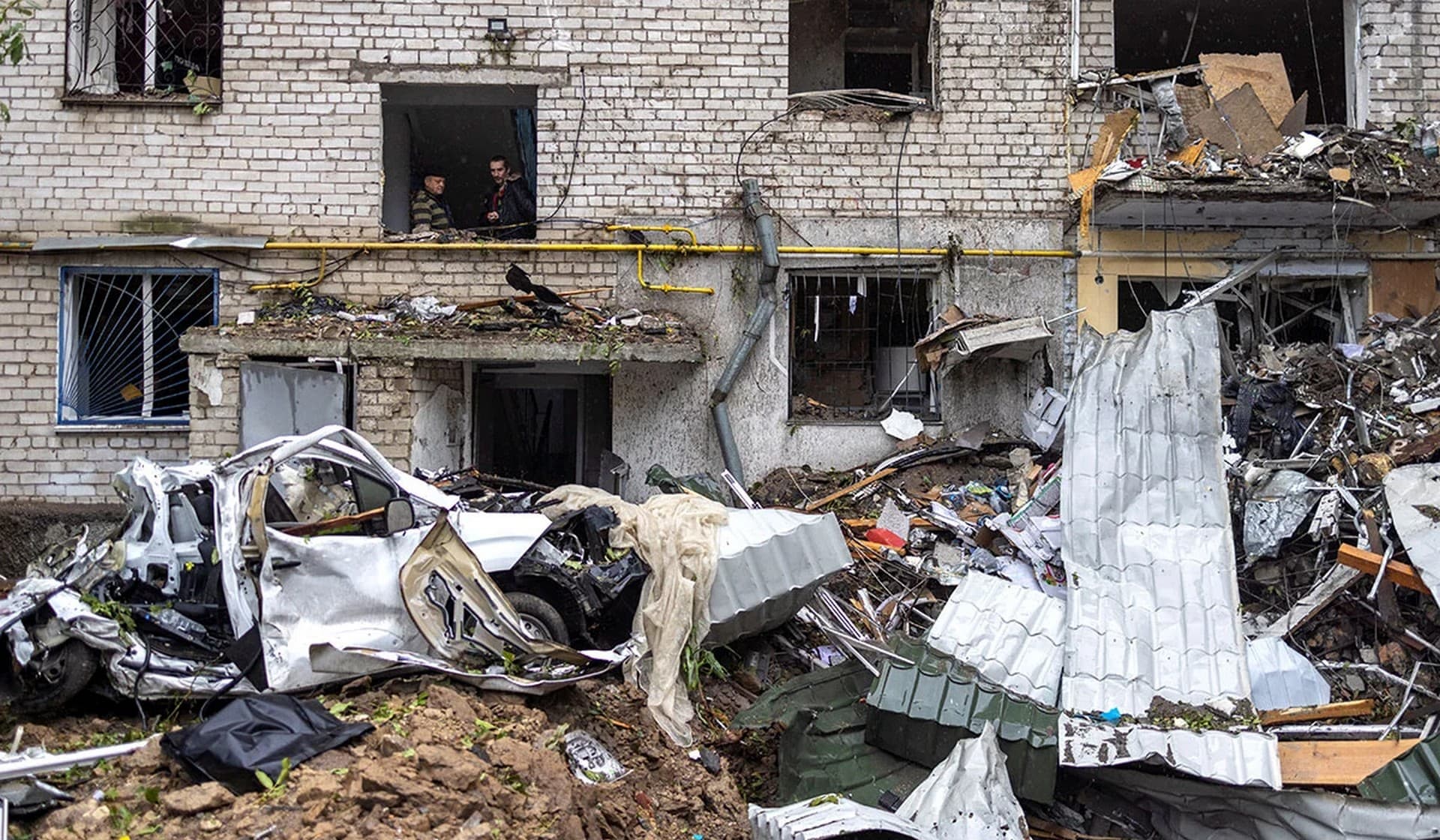 Men watch the scene and smoke at a residential building destroyed by a strike in Mykolaiv