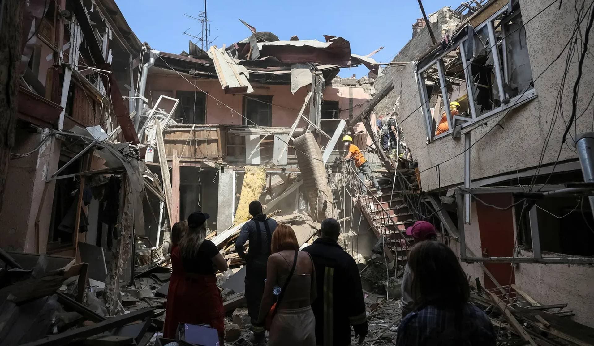Workers clean an area as residents stand nearby at the site of the apartment building hit by a Russian drone strike in Odesa