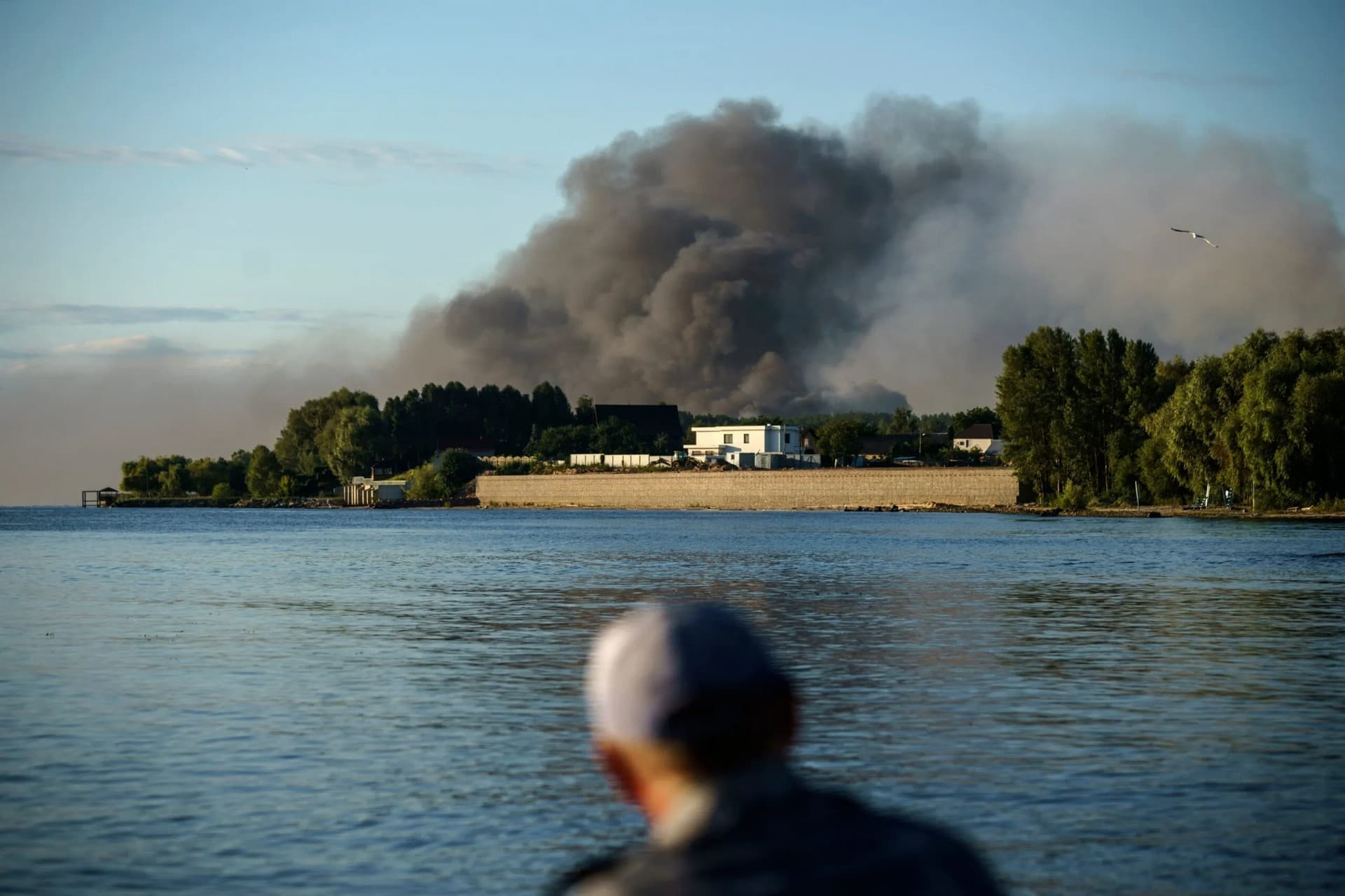 A fisherman watches smoke rise after Russian forces launched a missile attack on a military unit in the Vyshhorod district on the outskirts of Kyiv