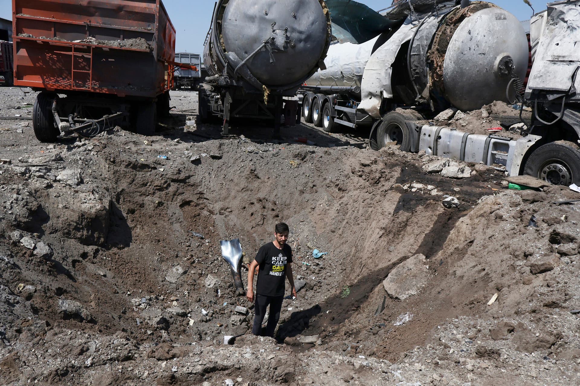 A man stands inside a crater next to destroyed trucks after Russian shelling in Rozumivka