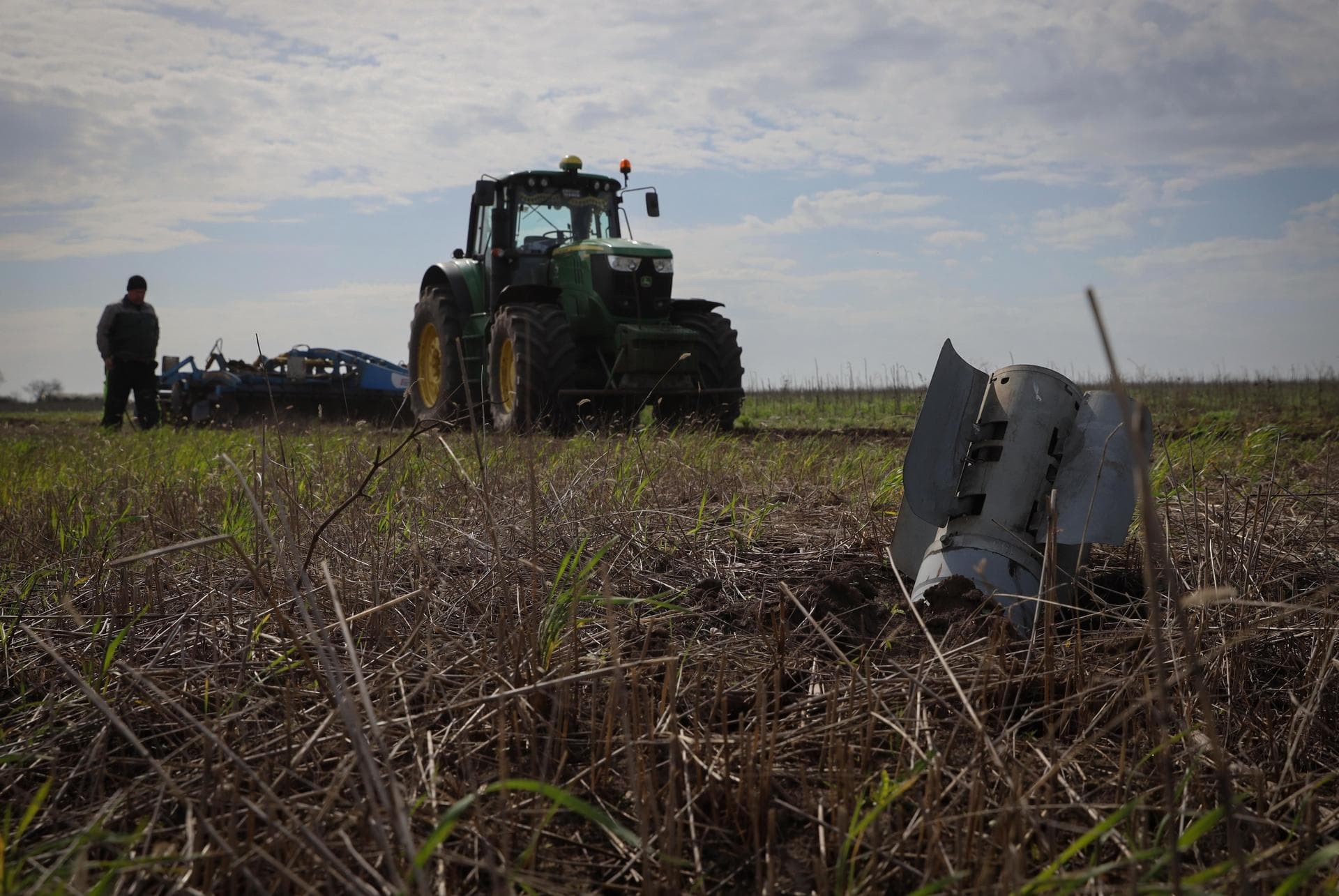 A part of a Russian rocket is seen in an agricultural field as a farmer works on a tractor during the sowing campaign in the Zaporizhzhia region